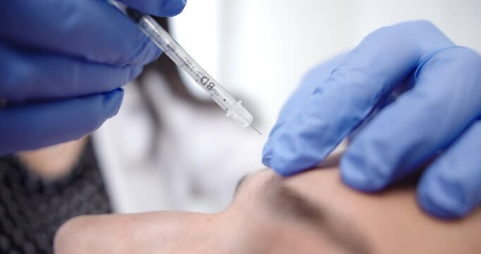 Beautiful super close-up shot of a patient being injected with cosmetic medicine in a dermatology clinic by a female doctor wearing blue gloves.