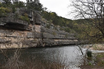 Reflecting stream by rocky cliff with forest trees in Lost Maples State Park, Texas