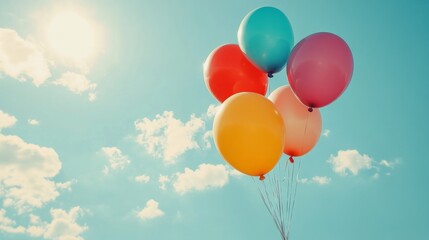 Five colorful balloons float against a bright blue sky with white clouds.