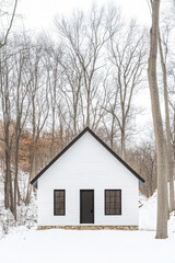 Simple white cabin surrounded by bare trees in a tranquil winter landscape