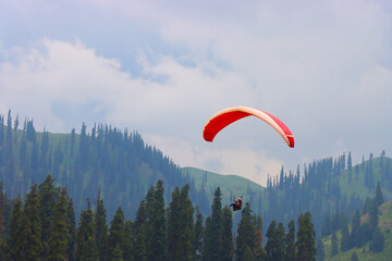 Paraglider soaring above a mountainous forest landscape, surrounded by trees and green hills, capturing the thrill and freedom of paragliding in nature