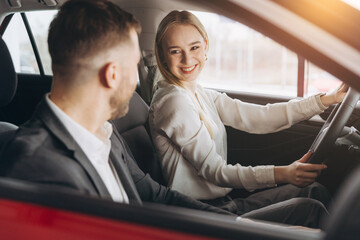 Competent car dealer showing female customer interior of luxury auto. Caucasian man and woman sitting inside and talking. Concept of selling and purchase.