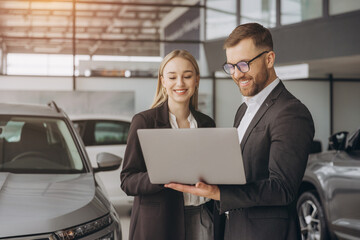Portrait of two workers with laptop inside car showroom