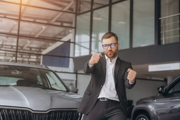 Yes, that's my new car! Customer in car dealership. Happy bearded man new car owner shows driving a car