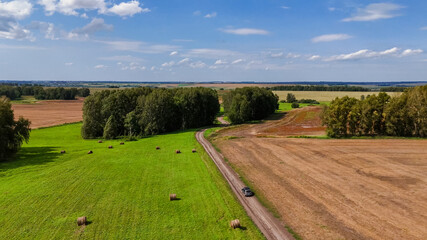 a green meadow field with rolls of hay and a country road on which the car is driving