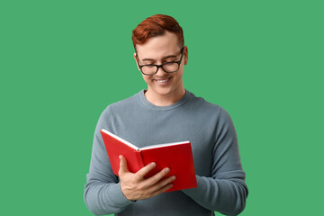 Young man in eyeglasses reading book on green background
