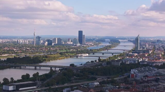 Urban sprawl intertwines with nature as the Danube River flows through Vienna. An aerial view highlights the city's skyline, bridges, and lush green spaces