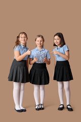 Cute girls in school uniform pointing at molecular model and showing thumb-up on beige background