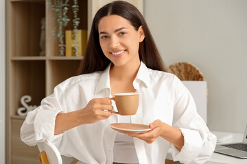 Pretty young woman with cup of hot coffee at home
