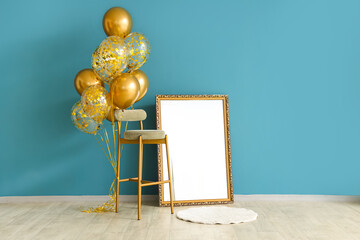 Golden air balloons, stool and blank photo frame near blue wall in room