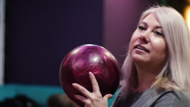 smiling beautiful caucasian woman blonde 40-49 years old holding bowling ball in hands getting ready to throw at pins, cheerful woman playing bowling