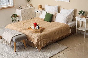 Interior of stylish bedroom with tables, bench and breakfast on bed