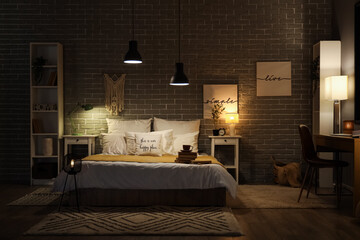 Interior of dark bedroom with glowing lamps, coffee cup and books on bed at night