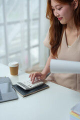 Fototapeta premium Asian businesswoman calculates company sales with a calculator Online financial information on laptop and tablet at desk in modern office.