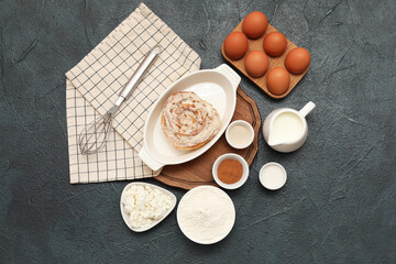 Baking dish with sweet cinnamon roll and different ingredients on dark background