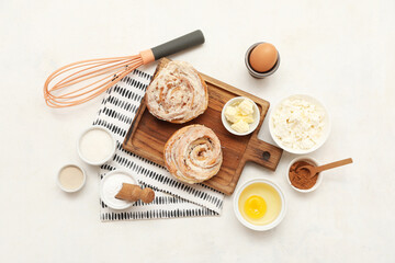 Wooden board with sweet cinnamon rolls and different ingredients on white background