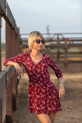 Portrait of a beautiful blonde girl in a red dress on a ranch.