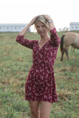 Portrait of a beautiful blonde girl in a red dress on a ranch.