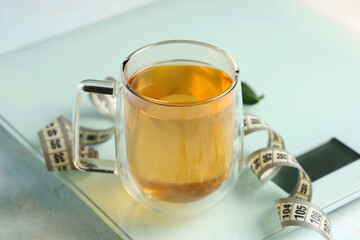 Cup of diet tea, measuring tape and scales on light background. Weight loss concept