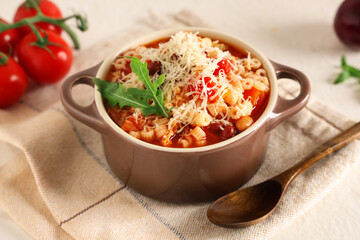 Bowl of pasta fagioli with cheese, arugula and tomatoes on white background