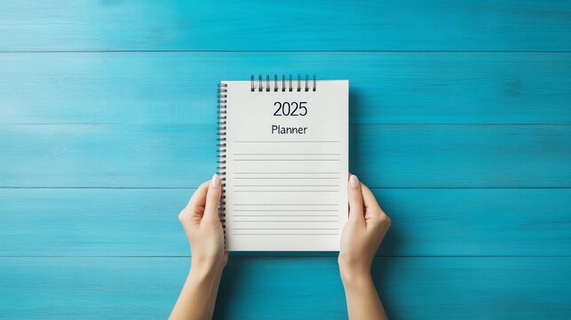 Hands holding a 2025 planner on a blue wooden table.