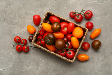 Wicker box with different fresh tomatoes on grey background