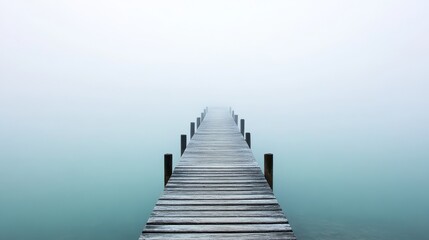 Fototapeta premium A serene wooden pier extends into a foggy, tranquil body of water, evoking calm and solitude.