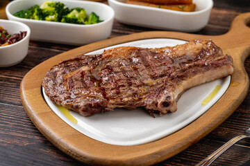 Grilled veal chop on white porcelain plate on wooden table