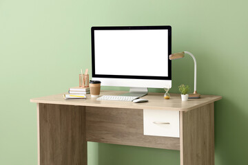 Stylish workplace with modern computer, cup of coffee, lamp and stationery near green wall in office