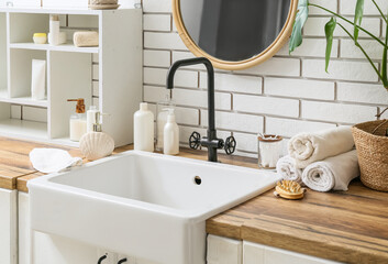 Bath supplies, shelf and sink on table near white brick wall in bathroom