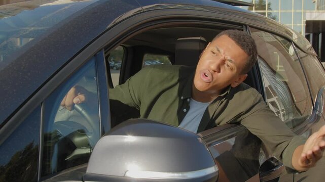 Aggressive nervous black male driver stuck in traffic jam, shouting at someone from car window, expressing irritation and anger while driving car in city during rush hour.