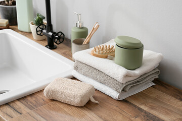 Bath accessories on wooden table near white wall in bathroom