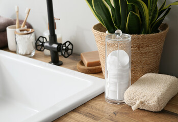 Bath accessories on wooden table near white wall in bathroom