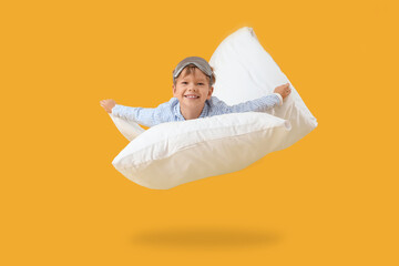 Cute little happy boy in pajamas with sleeping mask and pillow flying on yellow background