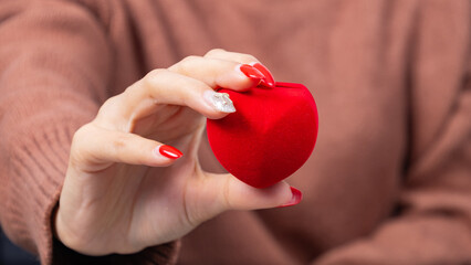 Asian woman wearing a brown shirt and holding a little red heart shaped gift box in hand. Red gift box, presents and gift boxes for festival and celebration.