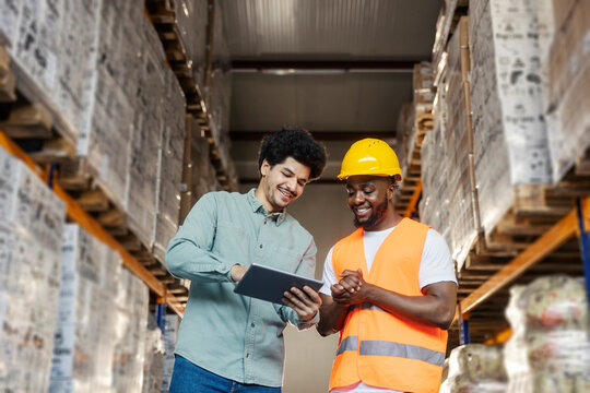 Interracial storage staff standing at warehouse and using tablet for tracking inventory and processes.