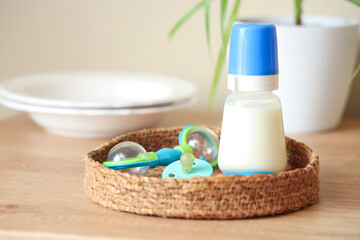 Wicker tray with bottle of baby milk formula, rattle, pacifier and plates on wooden kitchen counter