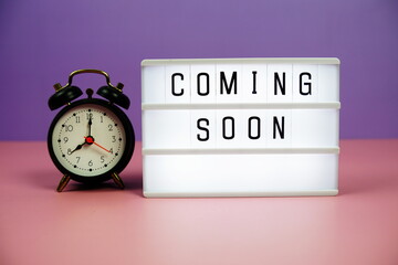 Coming Soon letterboard text on LED Lightbox and alarm clock on pink and purple background