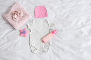 Composition with bottle of baby milk formula, clothes and accessories on light bed