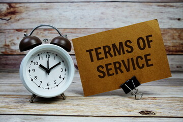 Terms of Service text on paper card with alarm clock on wooden background