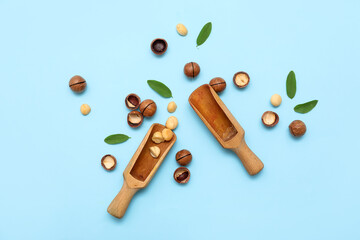 Wooden scoop with tasty macadamia nuts and leaves on blue background