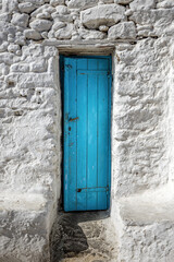 Old textured blue door in a white wall in Greece
