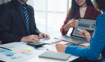 Strategic Business Meeting: A diverse team of professionals collaborates around a table, analyzing financial data on laptops and documents.  The image conveys focus, teamwork, and strategic planning.
