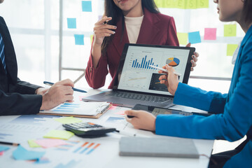 Business Data Analysis: Three professionals discuss financial charts on a laptop, showcasing a collaborative and insightful meeting in a modern office setting.
