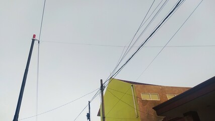 Directly below of residential buildings with electric poles and cables with a clear blue sky background