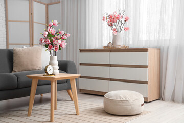 Comfortable sofa, coffee table and chest of drawers with magnolia flowers in room