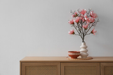 Vase with magnolia flowers on commode near grey wall