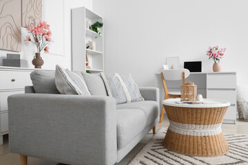 Interior of light living room with sofa, workplace and magnolia flowers in vase