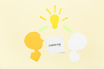 Paper human heads with word COACHING and light bulb on beige background