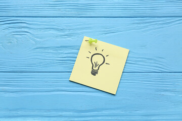 Paper with drawn light bulb and pin on blue wooden background. Coaching concept
